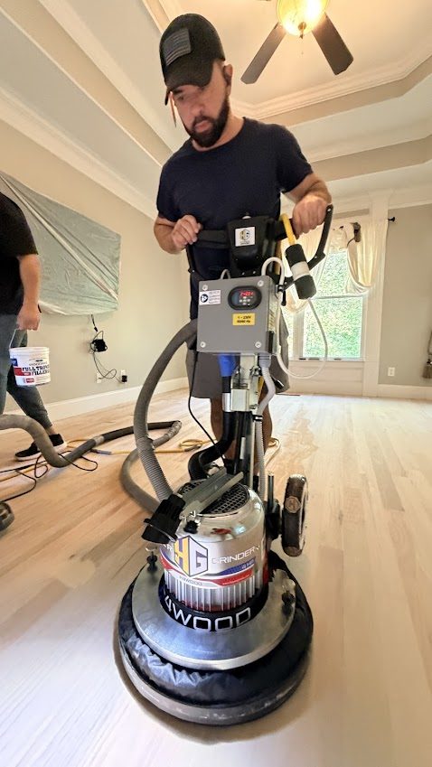 The Hardwood Guys crew sanding a floor with a commercial buffer during a refinish