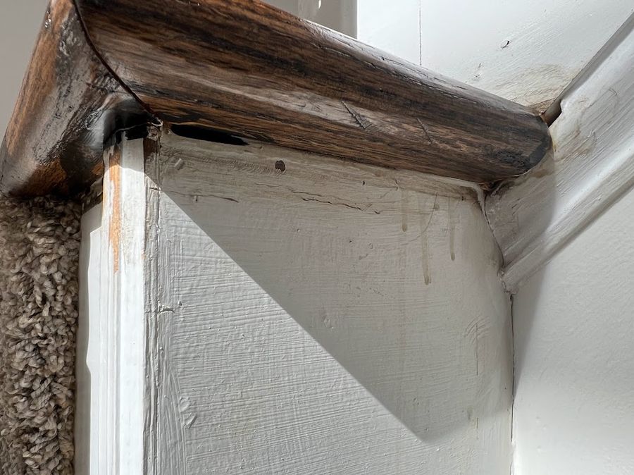 Stain drips on the wall and trim beside a newel post — normal during staining; needs paint touch-up.