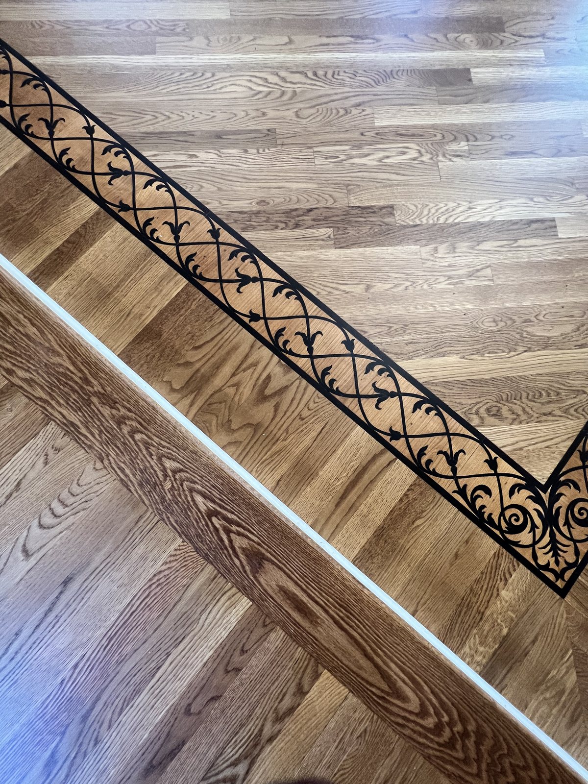 Close-up of a decorative wrought-iron scroll inlay border in a red oak hardwood floor, Golden Oak stain with matte finish