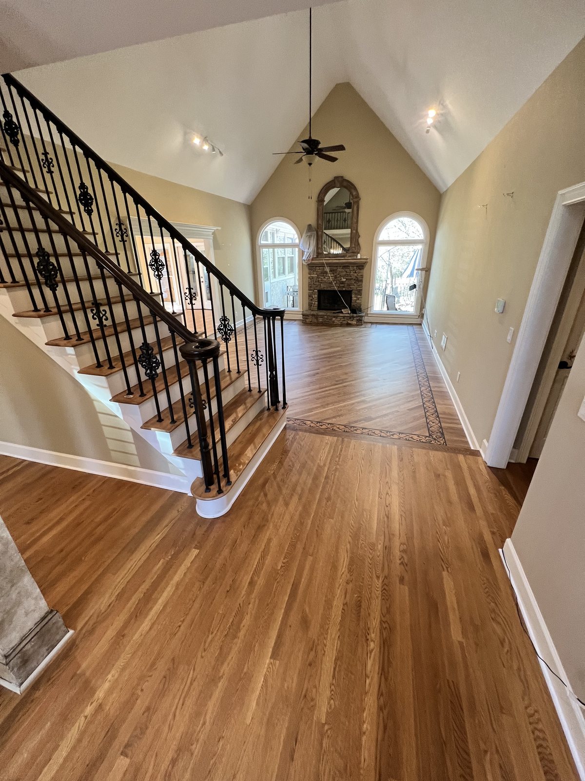 Grand foyer with red oak hardwood floor in Golden Oak stain and matte finish, staircase with wrought-iron balusters and stone fireplace
