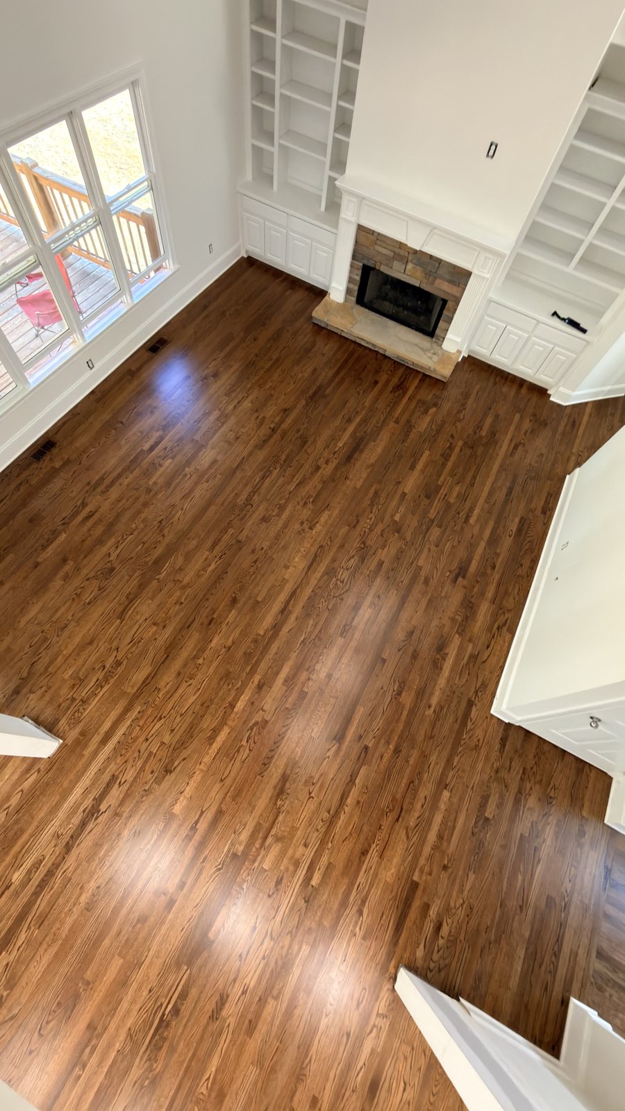 Living room with red oak hardwood floor in Honey stain and matte finish, stone fireplace and built-in shelving, aerial view
