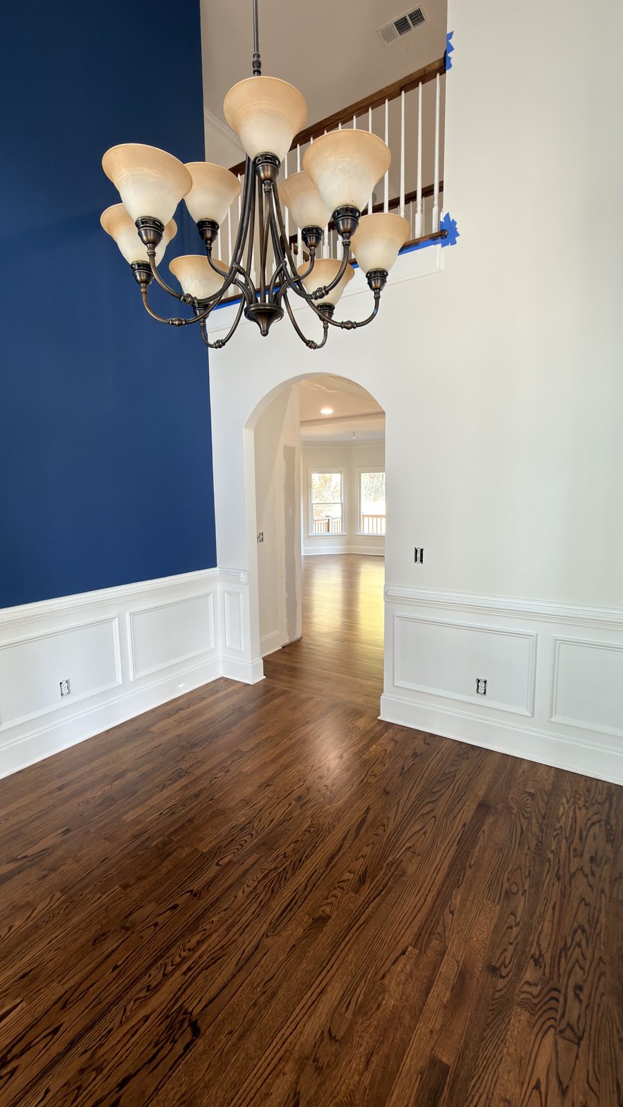 Entry hall with red oak hardwood floor in Honey stain and matte finish, chandelier, archway and navy accent wall