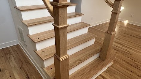 Box newel posts, stair treads and a curved handrail in natural-finish hardwood, installed by The Hardwood Guys over a matching hardwood floor